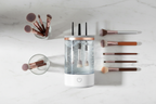 Veluné Aura Instant Brush Cleaner Pro flat lay with makeup brushes and glass bowl on marble