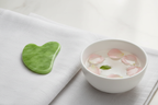 Veluné Aura Sculpting Gua Sha Stone on linen with floating petals
