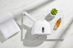 Veluné Aura Deep Clean Facial Steamer flat lay with towel, plant and serum on marble